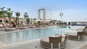 A pool area with lounge chairs and umbrellas, a Ferris wheel in the background, and a clear sky. - Spacious Dubai Marina 2BR | Great Views, Top Location (JBR)