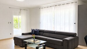 A modern living room with a sectional sofa, a glass coffee table, and a view of a balcony. - Holiday Home Nadalina (Vrgorac)