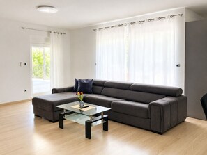 Een moderne woonkamer met een hoekbank, een glazen salontafel en uitzicht op een balkon.