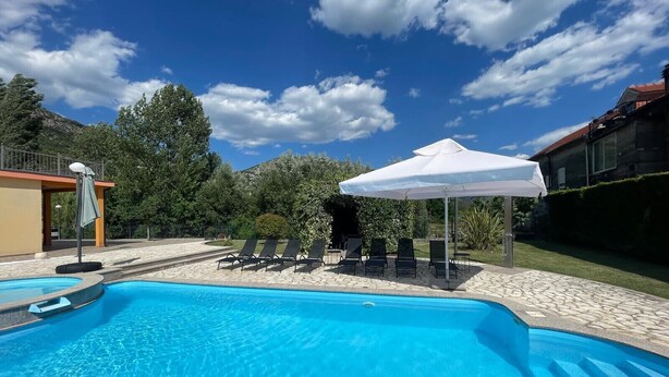 A swimming pool with lounge chairs and umbrellas, surrounded by trees and a building. - Holiday Home Nadalina (Vrgorac)