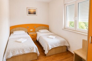 A bedroom with two single beds, a nightstand, a framed picture on the wall, and a window with blinds. - Holiday Home Nadalina (Vrgorac)