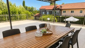 A wooden dining table with chairs, a glass bowl, and a candle on a patio with a view of a house and greenery. - Holiday Home Nadalina (Vrgorac)