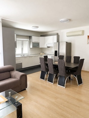 A modern kitchen with white cabinets, a built-in oven, and a refrigerator. There is a dining area with a glass table and chairs. - Holiday Home Nadalina (Vrgorac)