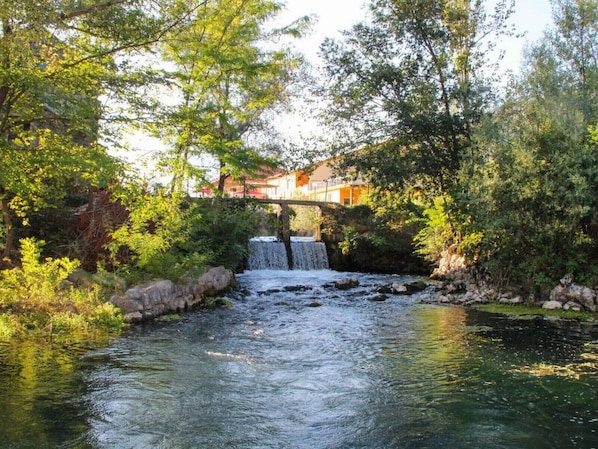 Una cascada pequeña en un área verde y exuberante, con un puente sobre ella.