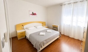 Une chambre d’hôtel bien rangée, avec un lit, des tables de chevet, une commode et une fenêtre avec des rideaux.