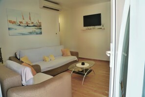 A living room with a sofa, a coffee table, a flat-screen TV mounted on the wall, and an air conditioning unit.