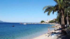 A beach with clear blue water, palm trees, and a few boats.