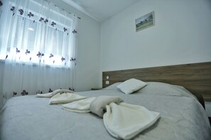 Una camera da letto con un letto, una finestra con tende leggere, una testiera in legno e un piccolo quadro appeso al muro.