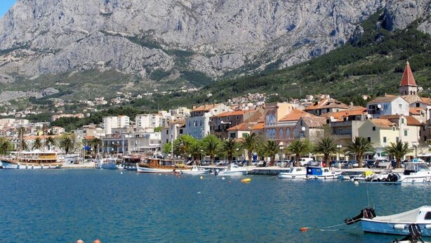 A coastal town with buildings, a marina, and a mountain backdrop.