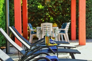 A patio area with lounge chairs, a table with a bottle and glass, and a chair with a basket of fruit.