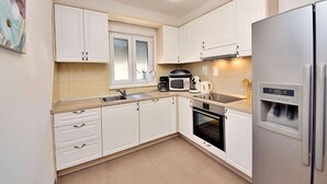 A modern kitchen with white cabinets, a stainless steel refrigerator, a microwave, a coffee maker, and an oven.
