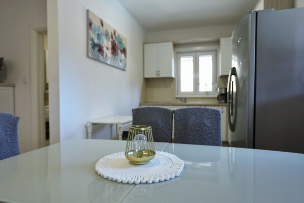 A modern kitchen with a stainless steel refrigerator, a dining table with a white placemat, and a painting on the wall.
