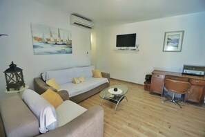 A living room with a sofa, a coffee table, a desk with a chair, and a television on the wall.