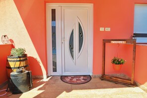 A door with a decorative glass panel, a welcome sign on a wooden stand, and a barrel with a plant.