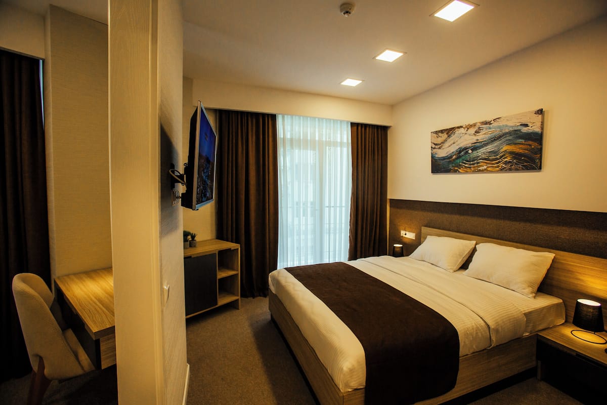 A hotel room with a bed, a desk, a chair, a TV, and a painting on the wall.