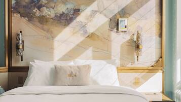 Une chambre d’hôtel avec un grand tableau abstrait au mur, un lit avec du linge de maison blanc et deux lampes fixées au mur.