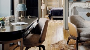 Une pièce comprenant un bureau, deux chaises, un lit, un miroir et une cheminée.