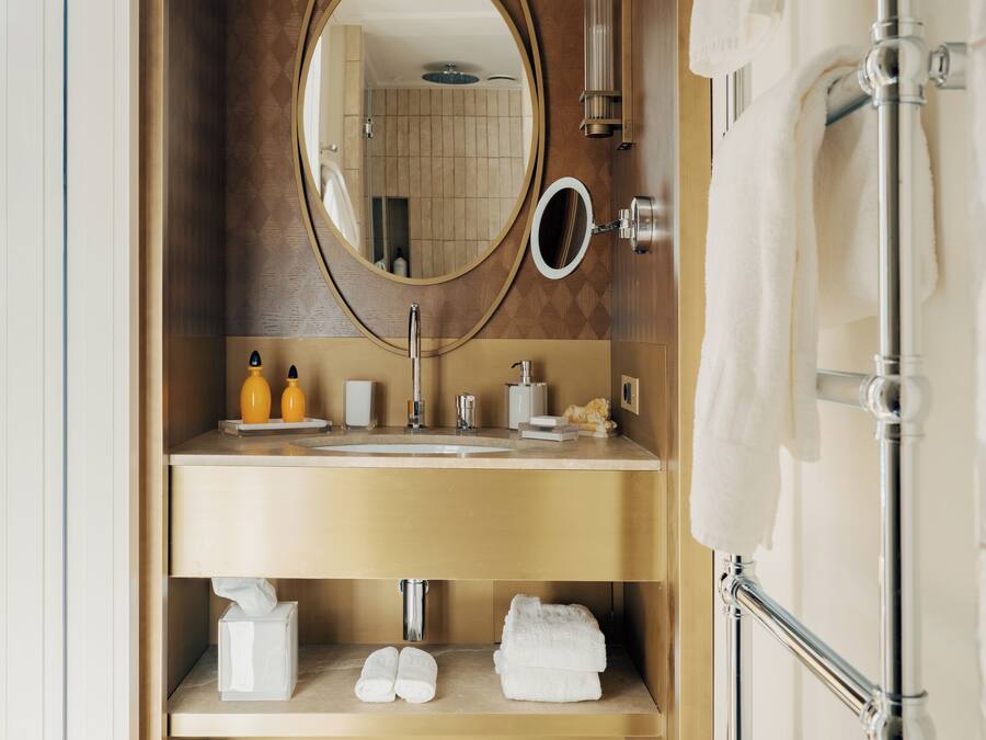 A bathroom with a wooden vanity, a round mirror, a towel rack, and a tiled floor.