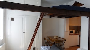A compact kitchen with a wooden table and chairs, a microwave, and a ladder leading to a lofted sleeping area. - Cœur de Ville & Sérénité: Your haven of peace in the heart of town! (Toulouse)