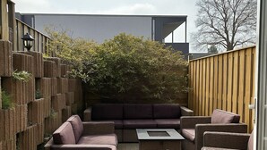 A patio area with wicker furniture, a built-in seating area, and a wooden fence. - 20 minutes to Amsterdam (Almere)