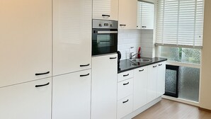 A modern kitchen with white cabinets, a black countertop, and a window with blinds. - 20 minutes to Amsterdam (Almere)