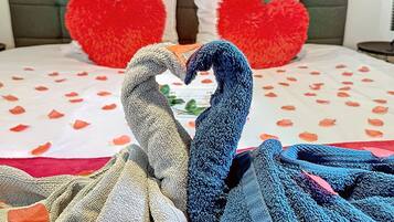 A bed with a heart-shaped pillow arrangement and a decorative swan made of towels.