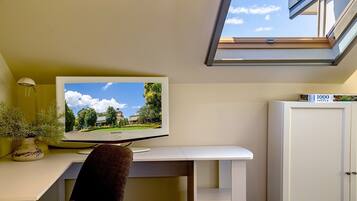 Een kamer met een bureau, een flatscreen televisie aan de muur, een kamerplant en een dakraam.