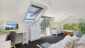 A spacious loft bedroom with a skylight, a large window, a desk, a comfortable seating area, and a view of the outdoors. - Centennial View Apartment – stylish comfort and stunning scenery for the perfect holiday escape (Bowral)