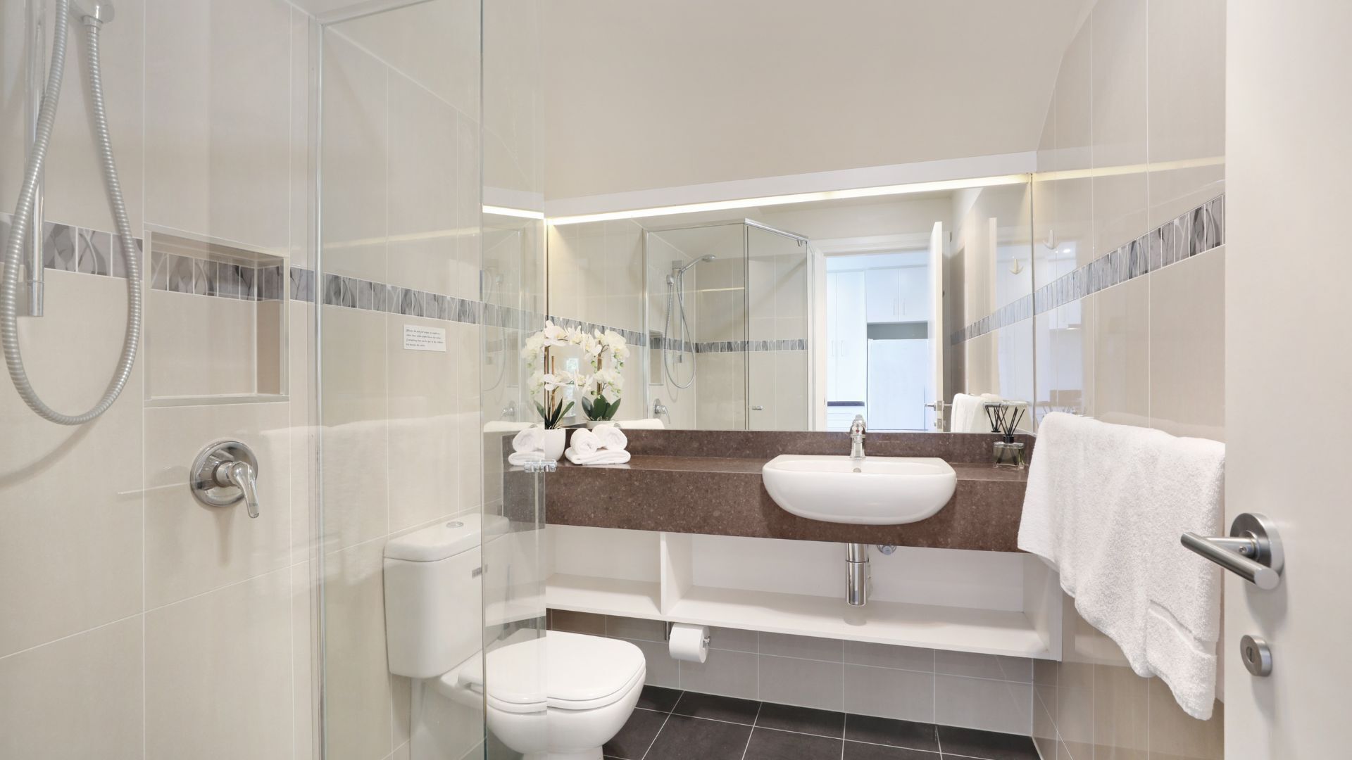 A modern bathroom with a glass shower enclosure, a white toilet, a sink with a mirror above it, and a towel rack.