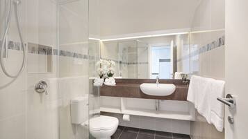 A modern bathroom with a glass shower enclosure, a white toilet, a sink with a mirror above it, and a towel rack.