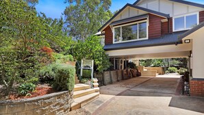 A two-story house with a covered driveway and a landscaped garden. - Centennial View Apartment – stylish comfort and stunning scenery for the perfect holiday escape (Bowral)