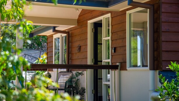 A wooden house with a covered porch, a sliding glass door, and a view of a garden. - Centennial View Apartment – stylish comfort and stunning scenery for the perfect holiday escape (Bowral)