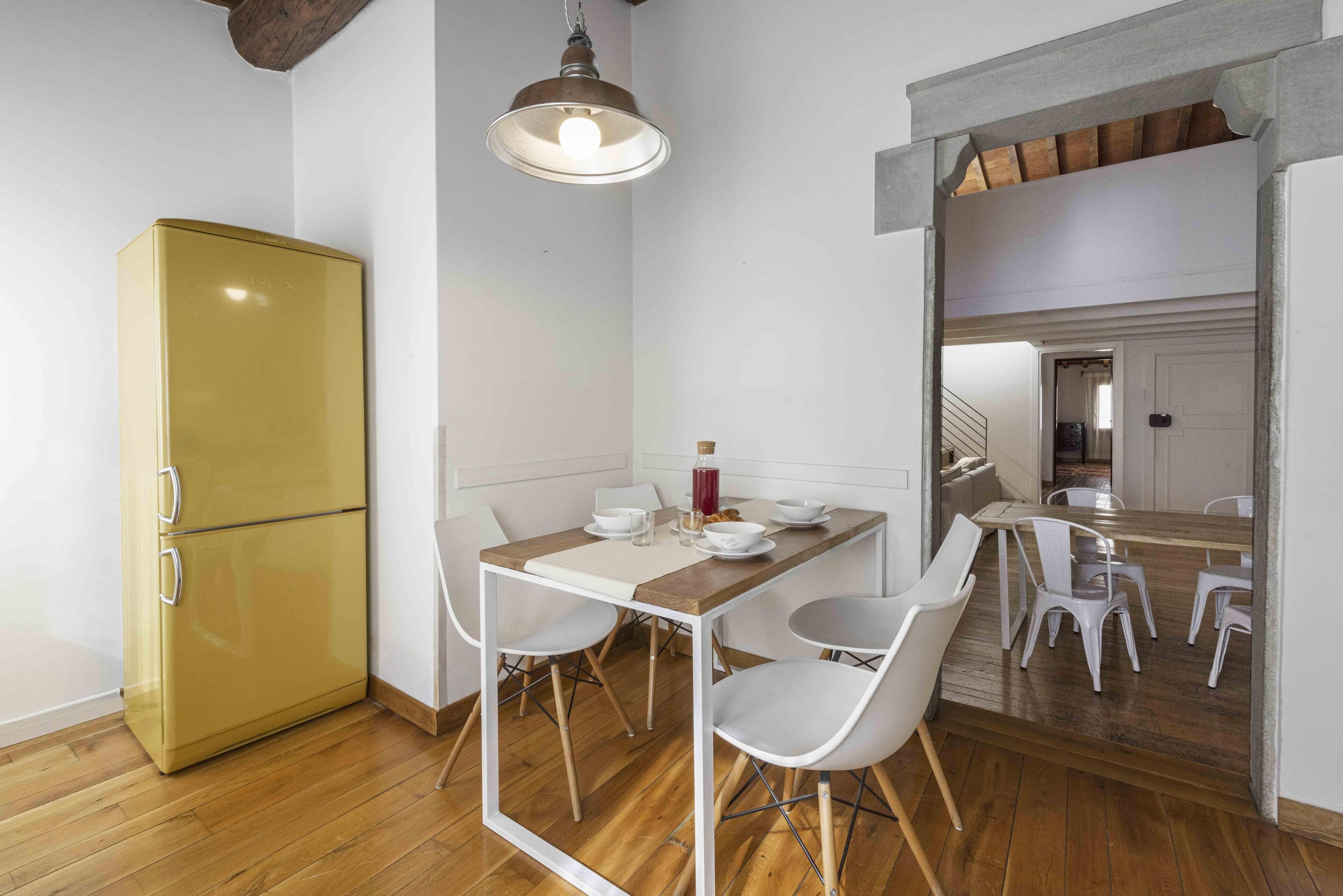 Une cuisine de taille réduite avec une table en bois, des chaises blanches et un réfrigérateur jaune.