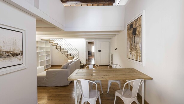 A spacious room with a wooden dining table, white chairs, a staircase, and a sofa. - Loft al Conventino by MMega (Florence)