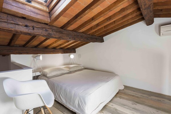 Une chambre avec un plafond en pente, un lit, un bureau et une chaise.