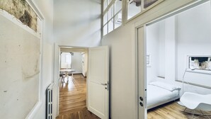 A narrow hallway with wooden flooring leading to a bedroom with a bed and a white chair. - Loft al Conventino by MMega (Florence)