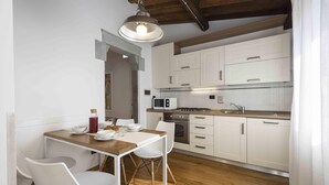 A compact kitchen with white cabinets, a wooden table, and two white chairs. - Loft al Conventino by MMega (Florence)