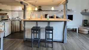 A kitchen with a central island, two stools, a tiled backsplash, and wooden beams on the ceiling. - Le petit gite dans la prairie (Revel)