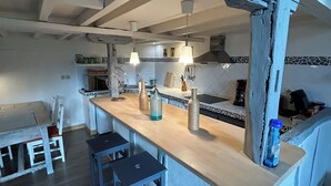 A kitchen with a wooden island, bar stools, hanging pendant lights, and a tiled backsplash. - Le petit gite dans la prairie (Revel)