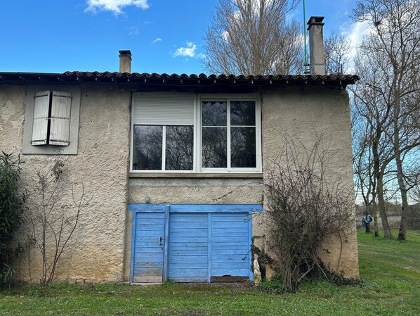 A rustic building with a tiled roof, a window with shutters, and a blue garage door. - Le petit gite dans la prairie (Revel)
