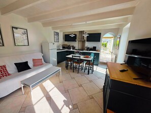 A modern living room with a white sofa, a dining table, and a kitchen area with a TV and a refrigerator.