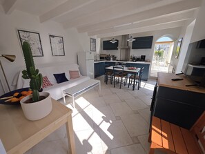 A modern kitchen with a dining area, a white sofa, and a cactus plant.