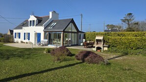 A modern house with a large glass conservatory, a patio with outdoor furniture, and a well-maintained garden.