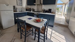 A modern kitchen with dark blue cabinets, a white countertop, and a dining table with four chairs. There is a large window providing natural light and a view of the outdoors.