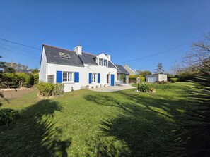 A two-story house with a white exterior and blue shutters, a covered patio, and a well-maintained lawn.
