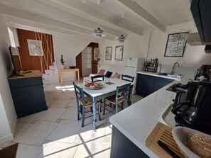 A modern kitchen with a central island, a dining area with blue chairs, and a staircase leading to an upper level.