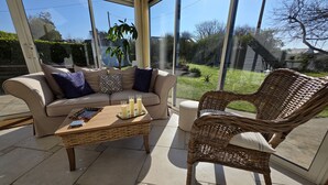 A sunlit patio with a beige sofa, a wicker chair, and a coffee table with candles.