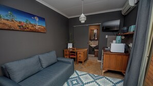 Un soggiorno con un divano grigio, un tappeto decorato, un quadro, una scrivania in legno, una televisione e un angolo cottura.