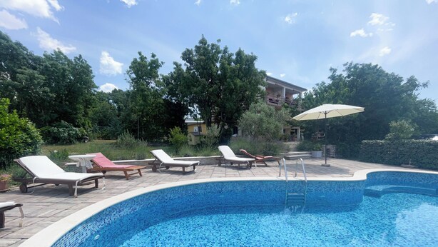 A swimming pool with tiled blue edges and a tiled floor, surrounded by lounge chairs and an umbrella. - Apartment Matkovic 4 (Jadranovo)