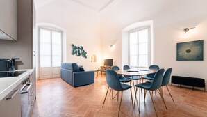 Eine moderne Wohnung mit Küche, Essbereich und Wohnzimmer. Sie verfügt über einen großen Esstisch mit Stühlen, eine Couch und einen Fernseher.